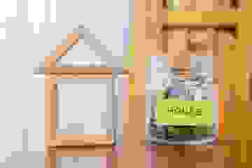 Savings jar for a house deposit beside a wooden house model