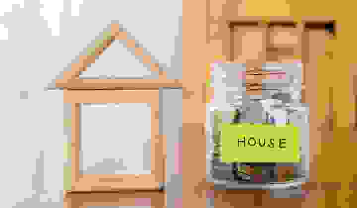 Savings jar for a house deposit beside a wooden house model