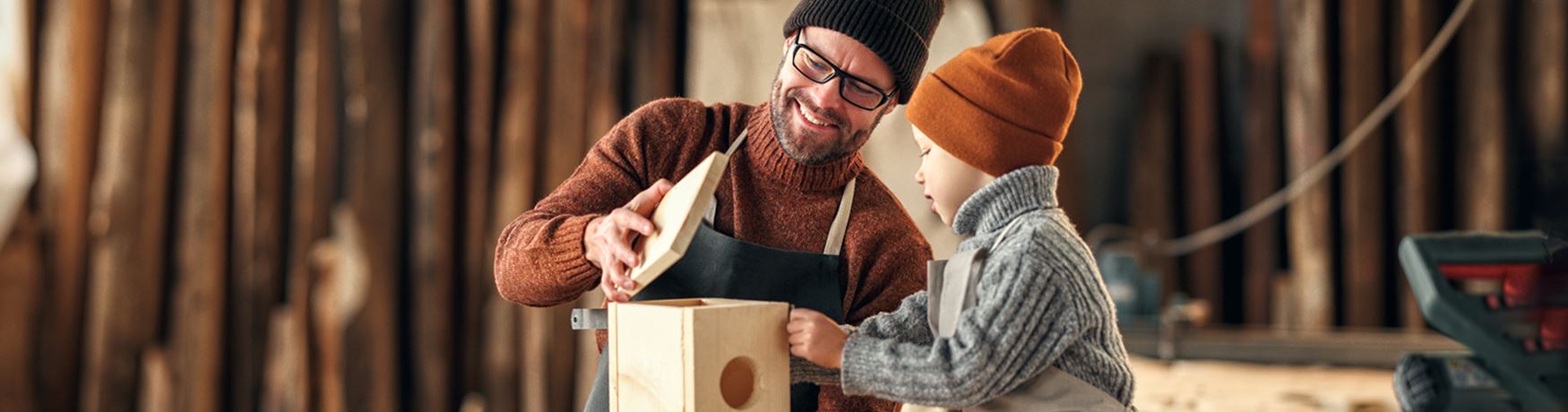 Self employed woodworker with his young son in his workshop making a birdhouse together