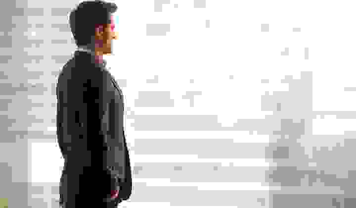 Business man stands looking out out a blurred window with hands in pockets