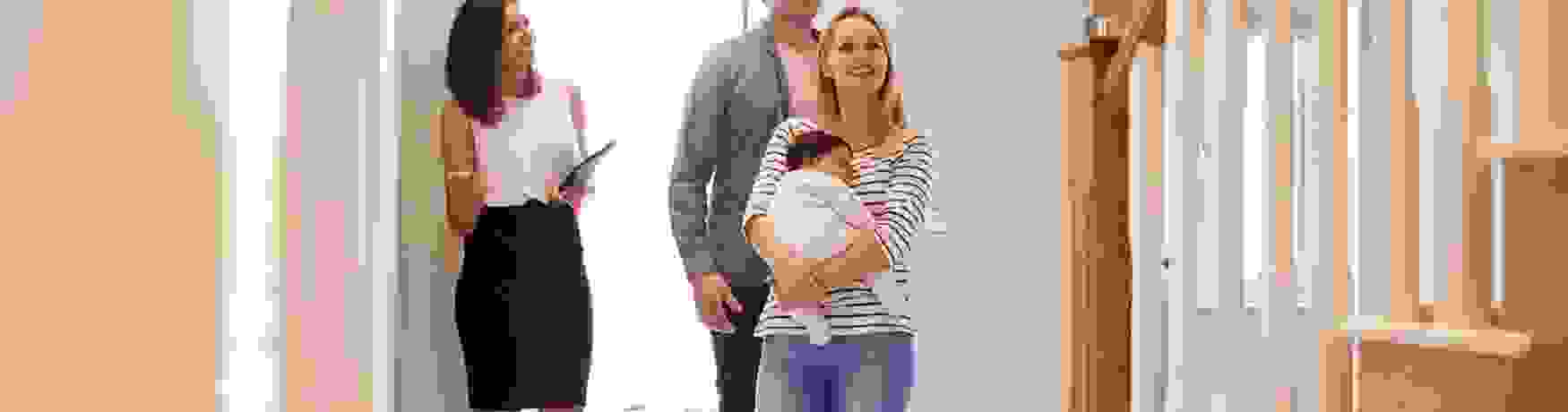 Young family with a baby walking into a house with a real estate agent