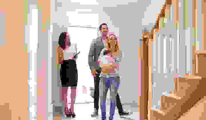 Young family with a baby walking into a house with a real estate agent