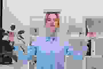 Woman standing balancing a book on her head with hands out and eyes closed