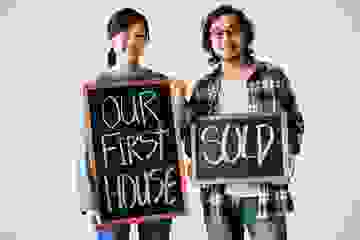 Young couple sand with blackboards announcing that they have sold their first house
