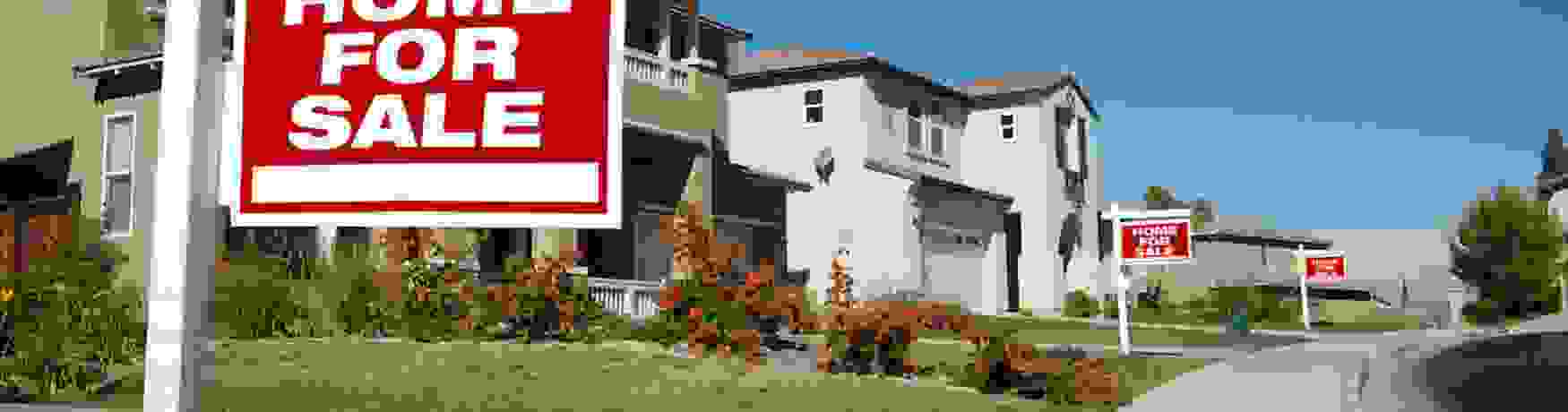 Suburban street with several For Sale signs outside properties in a row
