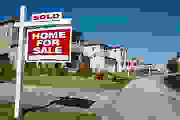 Suburban street with several For Sale signs outside properties in a row