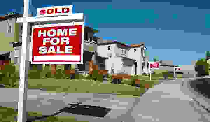 Suburban street with several For Sale signs outside properties in a row