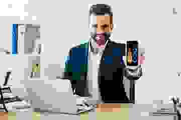 Young businessman in suit, with an open laptop and phone, showing us graphs