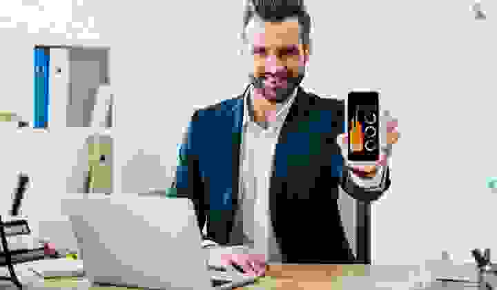 Young businessman in suit, with an open laptop and phone, showing us graphs