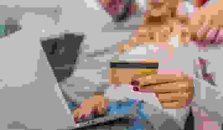 A soft focus image of a couple looking at a laptop holding a credit card in the foreground