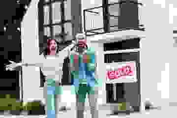 Cheerful man and woman celebrating near house and board with sold letters