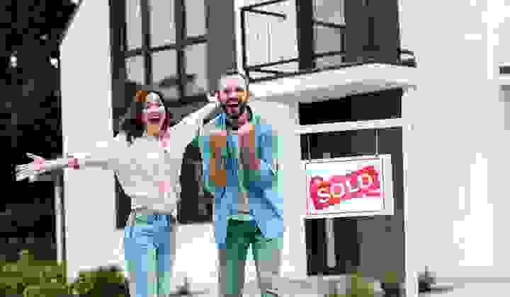 Cheerful man and woman celebrating near house and board with sold letters