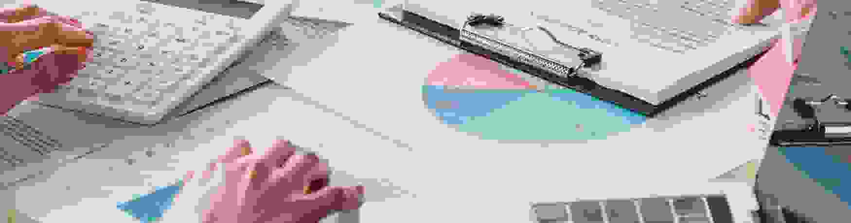 Close-up of graphs and loan agreements on a desk with laptops and two pairs of hands