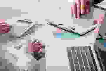 Close-up of graphs and loan agreements on a desk with laptops and two pairs of hands