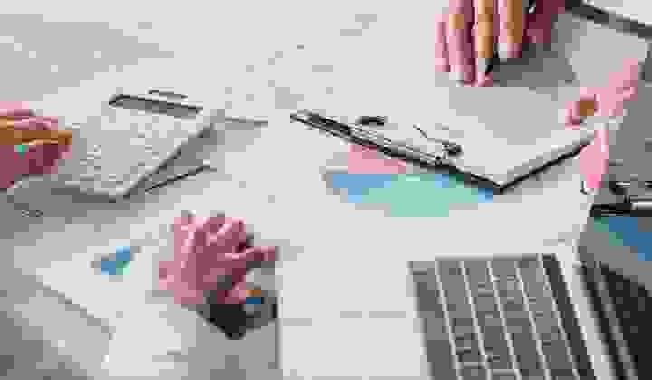 Close-up of graphs and loan agreements on a desk with laptops and two pairs of hands