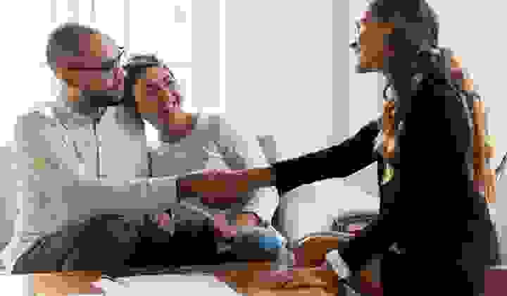 Happy young couple shaking hands with their mortgage adviser celebrating the purchase of their first home