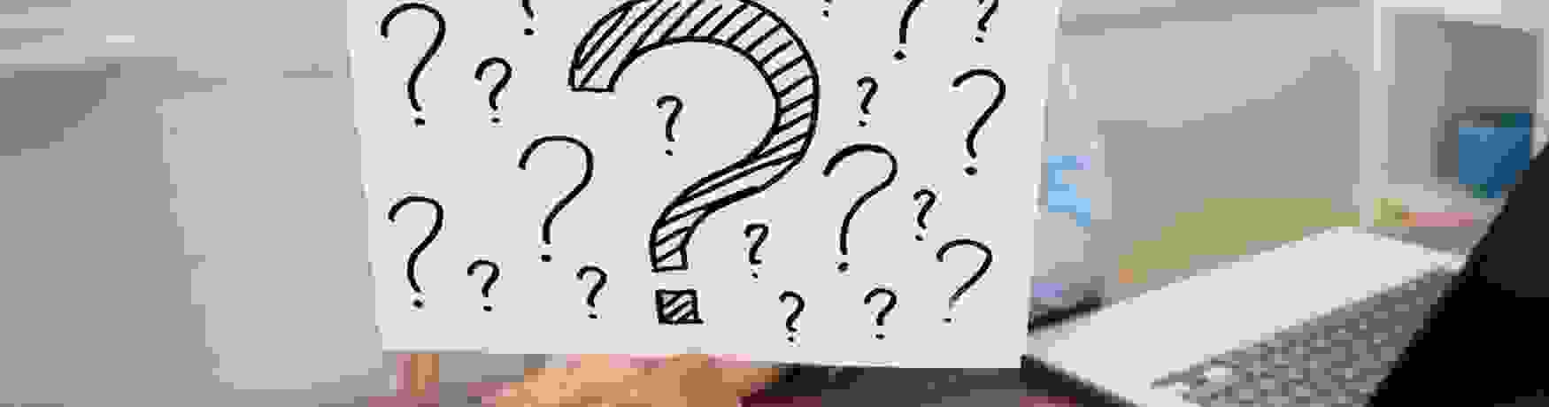 Woman at her desk with a calculator and laptop holding up a sign with lots of question marks