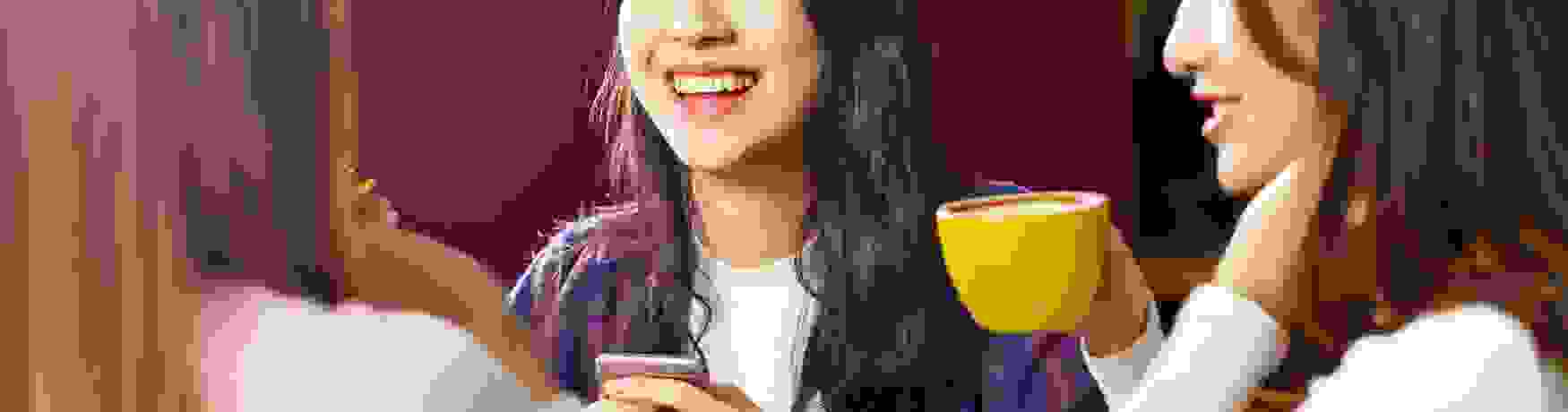 Three women at a cafe laughing and drinking coffee