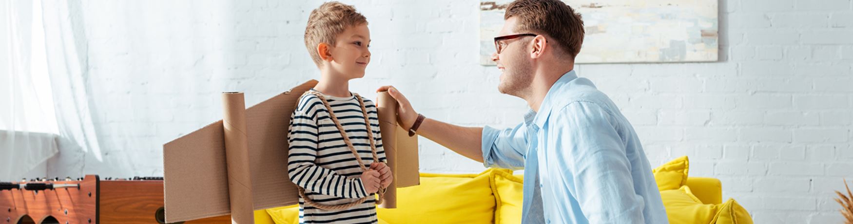Father talking to young son who is wearing home-made wings