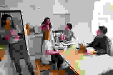 A group of laughing students gathered in a kitchen with laptops and sandwiches