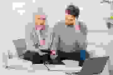 A couple sits on their couch with a calculator and folder looking at their financial statements