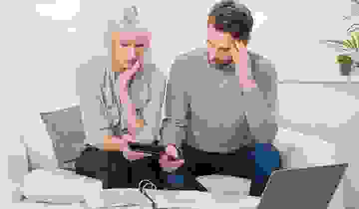 A couple sits on their couch with a calculator and folder looking at their financial statements