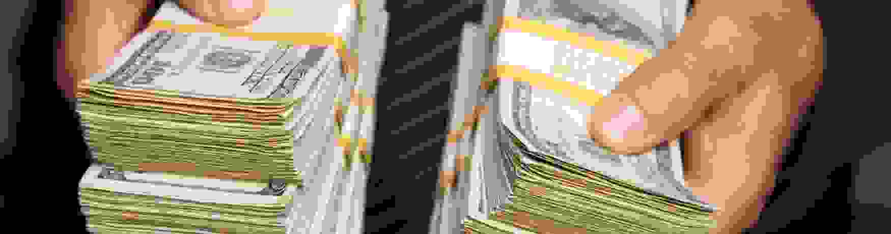 Close up photo of stacks of American notes being held by a man in a suit