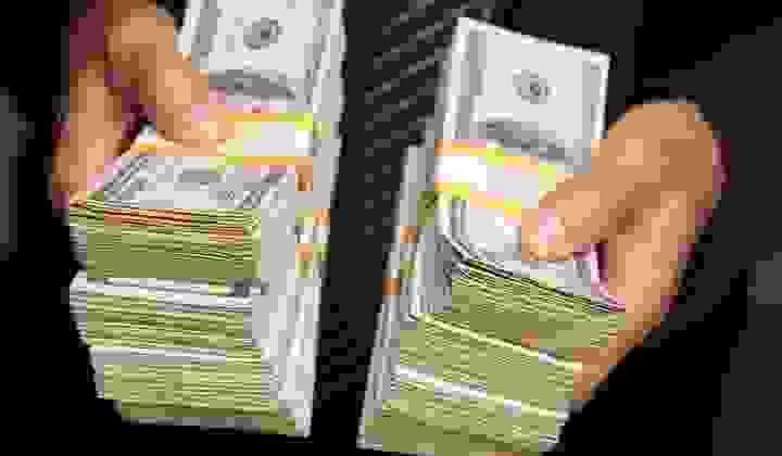 Close up photo of stacks of American notes being held by a man in a suit