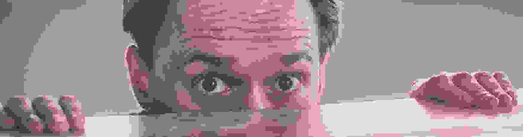 Nervous man peering over the edge of a wooden desk
