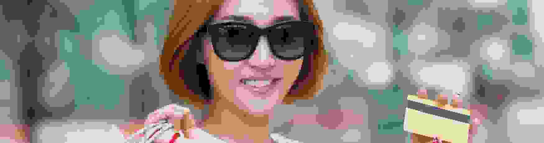 Smiling woman wearing sunglasses and holding lots of shopping bags and her credit card