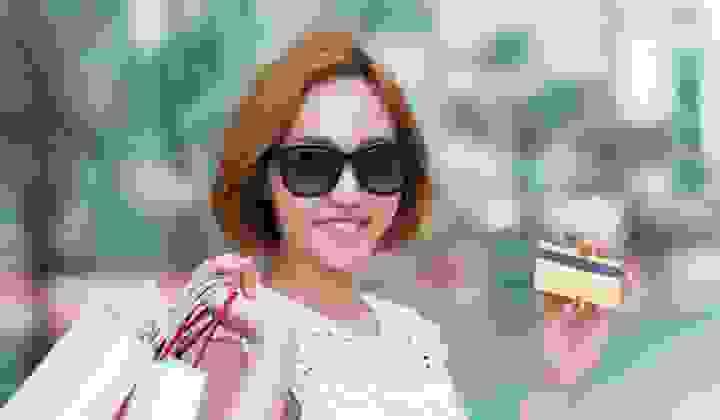 Smiling woman wearing sunglasses and holding lots of shopping bags and her credit card