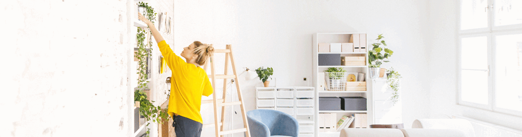 Young woman wearing a yellow jumper arranging plants on a shelf in her new home