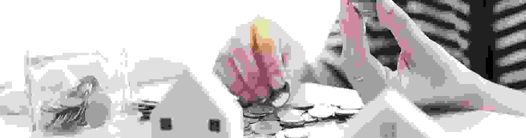 Soft focus of a woman holding a stack of coins with model houses and a jar of coins on a table