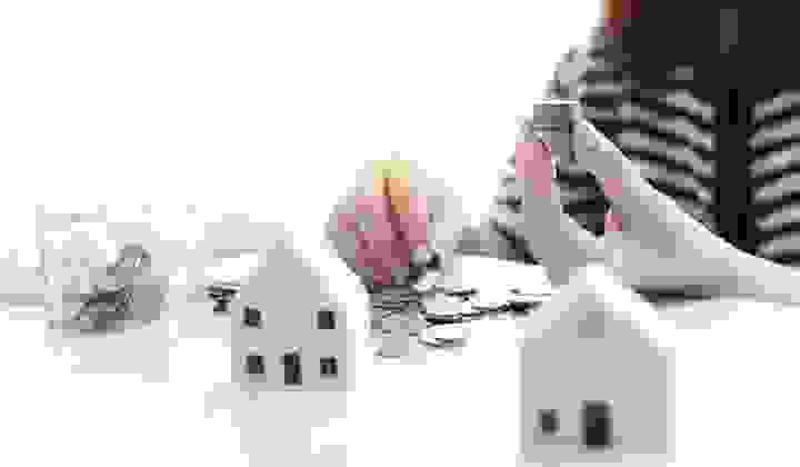 Soft focus of a woman holding a stack of coins with model houses and a jar of coins on a table