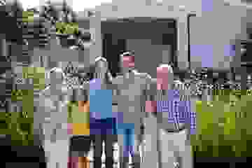 Smiling family standing with arms around each other outside a house