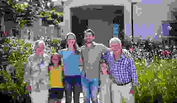 Smiling family standing with arms around each other outside a house