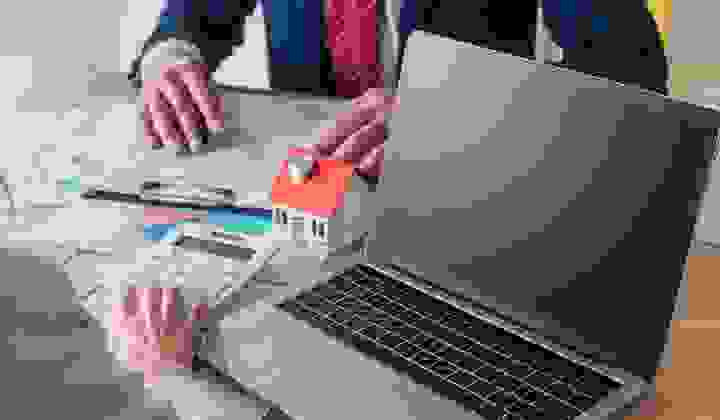 Two people looking over real estate paperwork with a calculator and open laptop