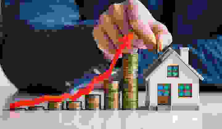 Growing stacks of coins with an arrow depicting inflation leads to a house with a man's hand holding a coin above a house model.