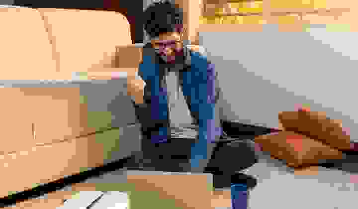 Man sitting cross legged in his lounge looking at his laptop and doing a fist pump