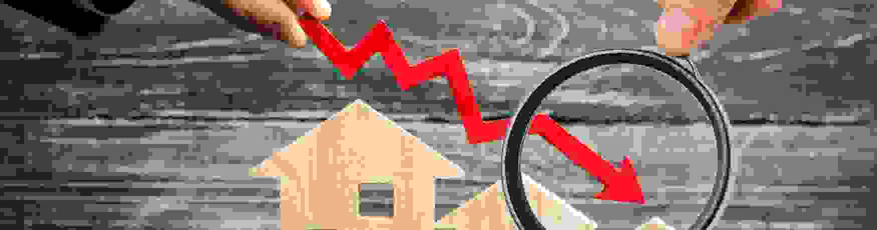 Magnifying glass over a red downward-pointing arrow and model houses showing the decrease in house prices