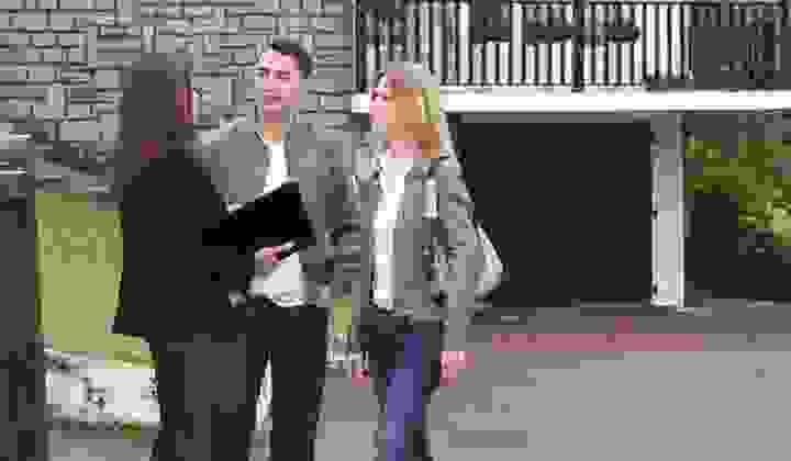 Couple discusses plans with a real estate agent outside a house