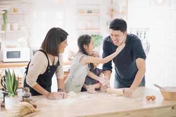 Young girl baking with her family and putting a floured handprint on her father's cheek and laughing
