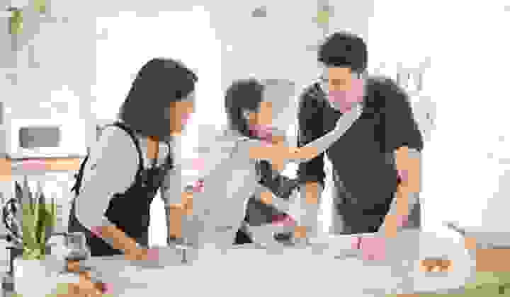 Young girl baking with her family and putting a floured handprint on her father's cheek and laughing