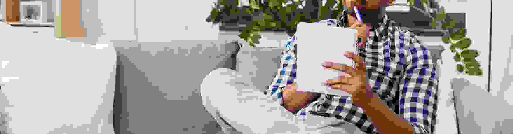 Young man sitting on his couch with pen and paper looking thoughtful