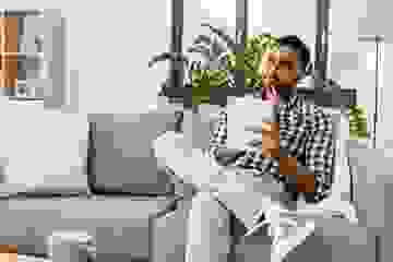 Young man sitting on his couch with pen and paper looking thoughtful