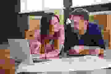 Happy couple lying on the floor with house plans and a laptop