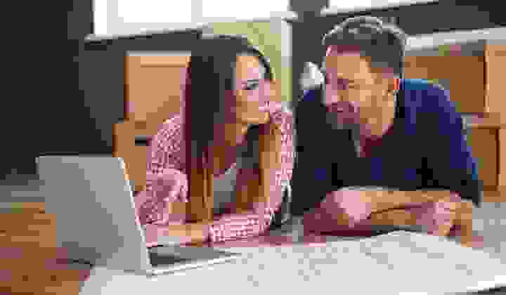 Happy couple lying on the floor with house plans and a laptop