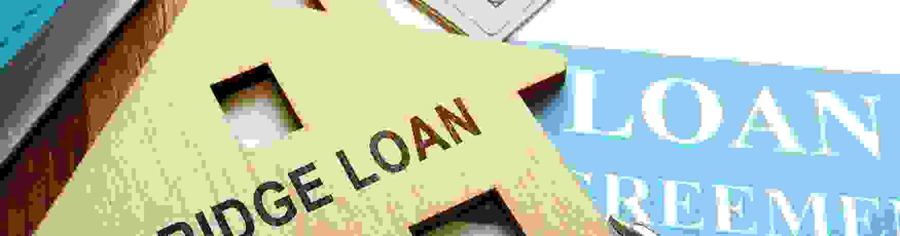 Close-up of paperwork, money, pen and a bridge loan wooden house