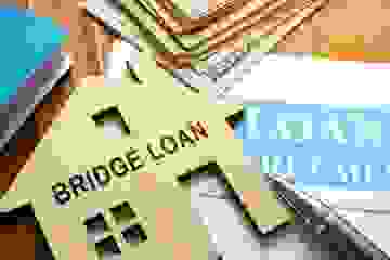 Close-up of paperwork, money, pen and a bridge loan wooden house