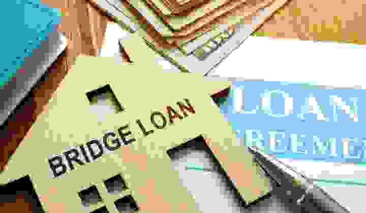 Close-up of paperwork, money, pen and a bridge loan wooden house